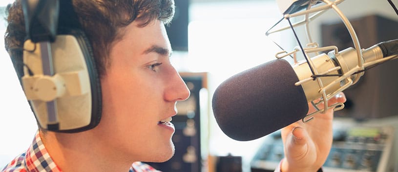 Young man speaks into microphone at a radio broadcast station. If you want to take radio and television broadcasting courses give us a call.